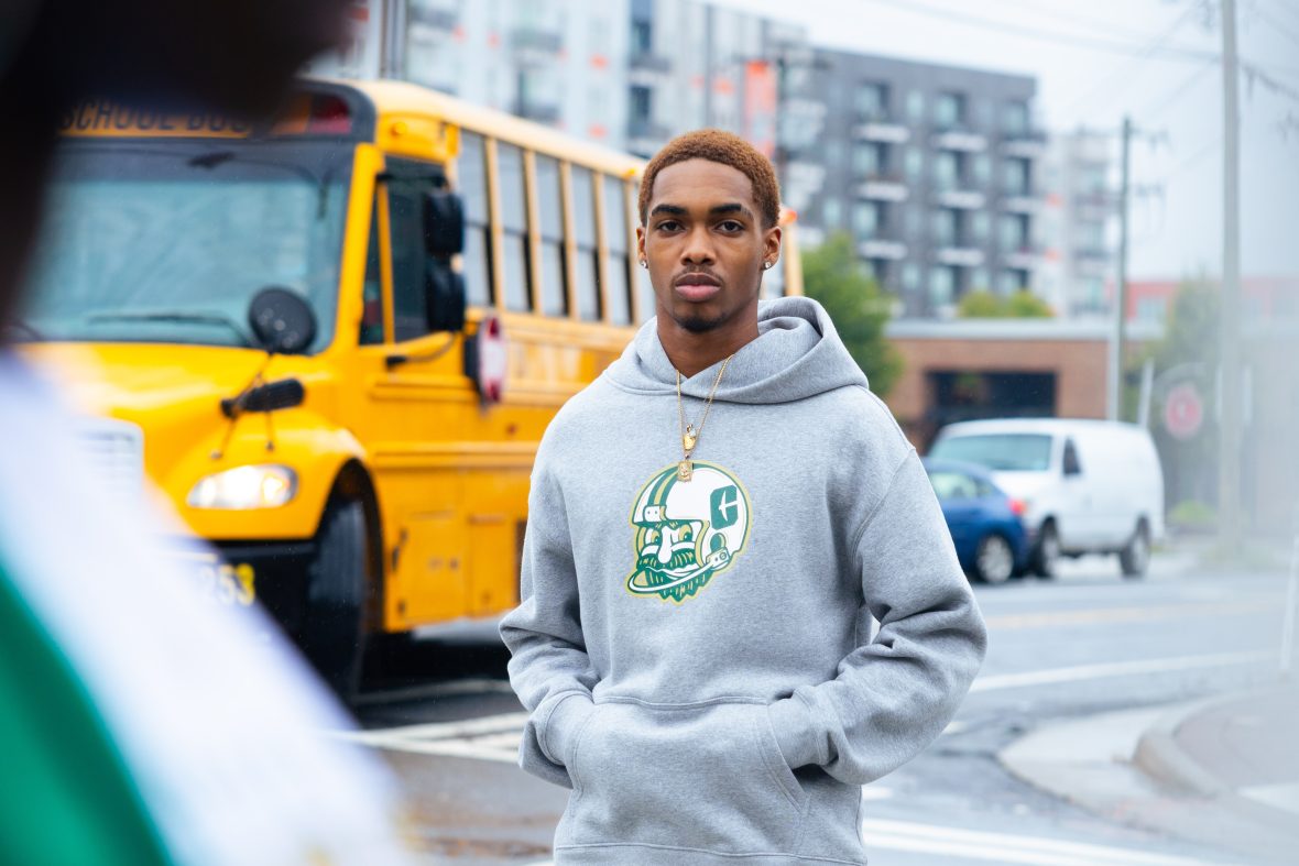 young man standing in front of street intersection wearing gray sweatshirt and jeans
