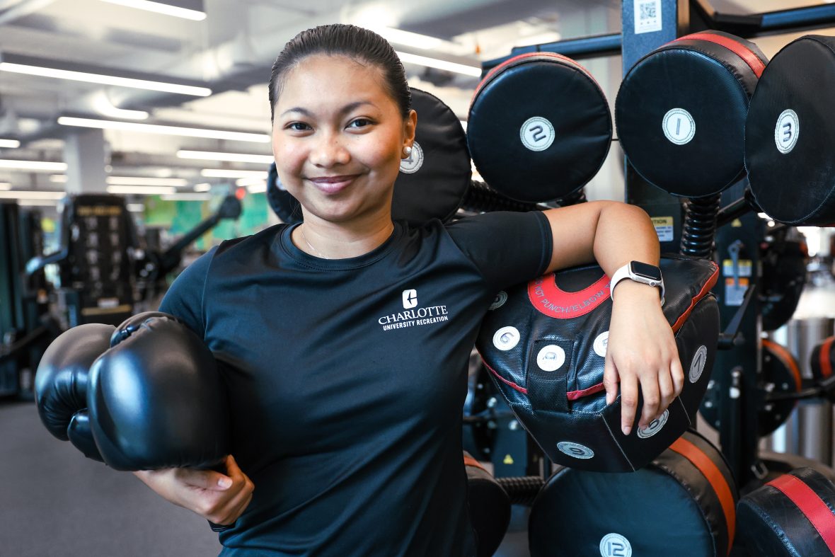 Student worker at the university recreation center wearing an athletic charlotte shirt and holding gym equipment